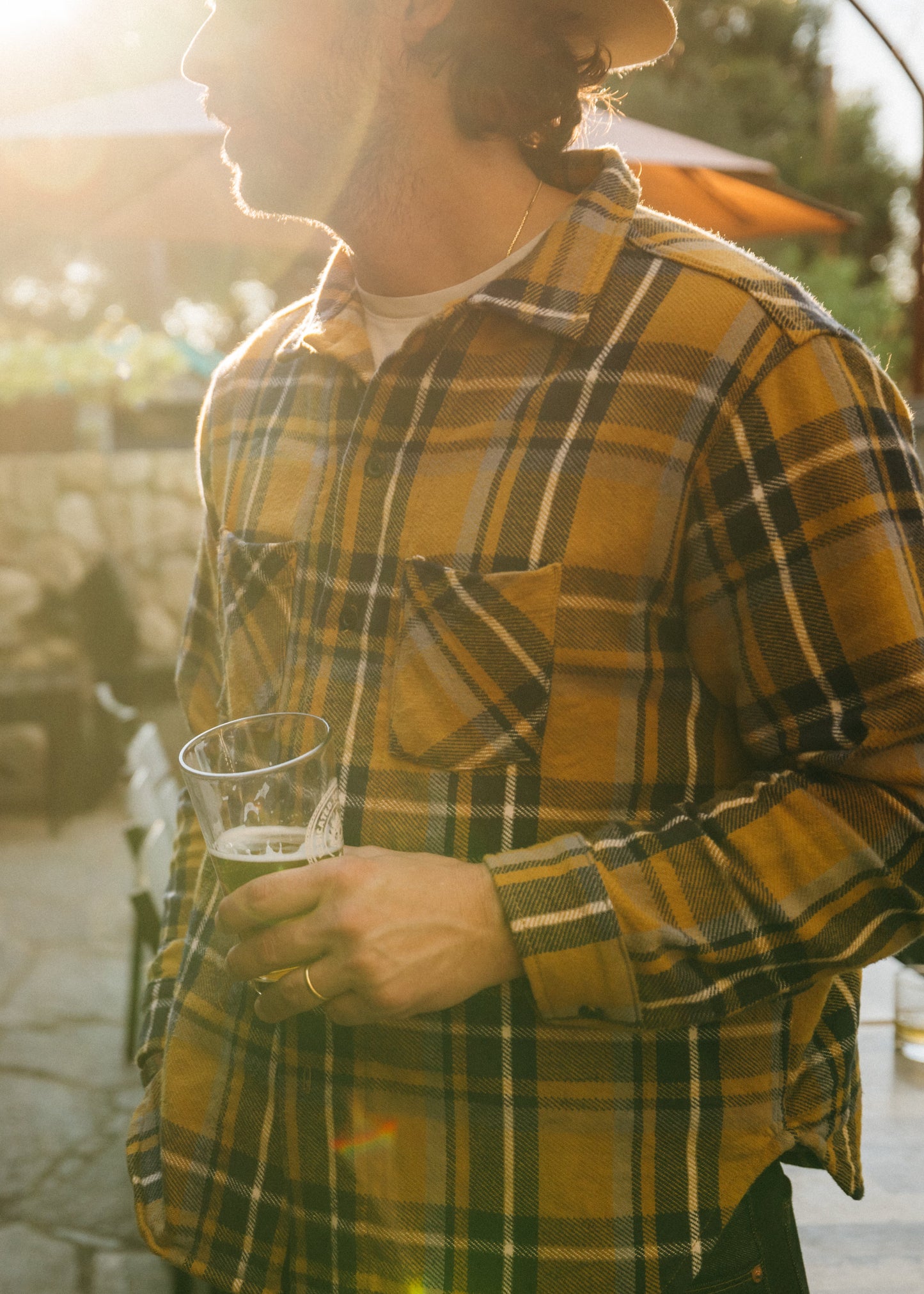 Man in a yellow plaid shirt holding a glass outdoors