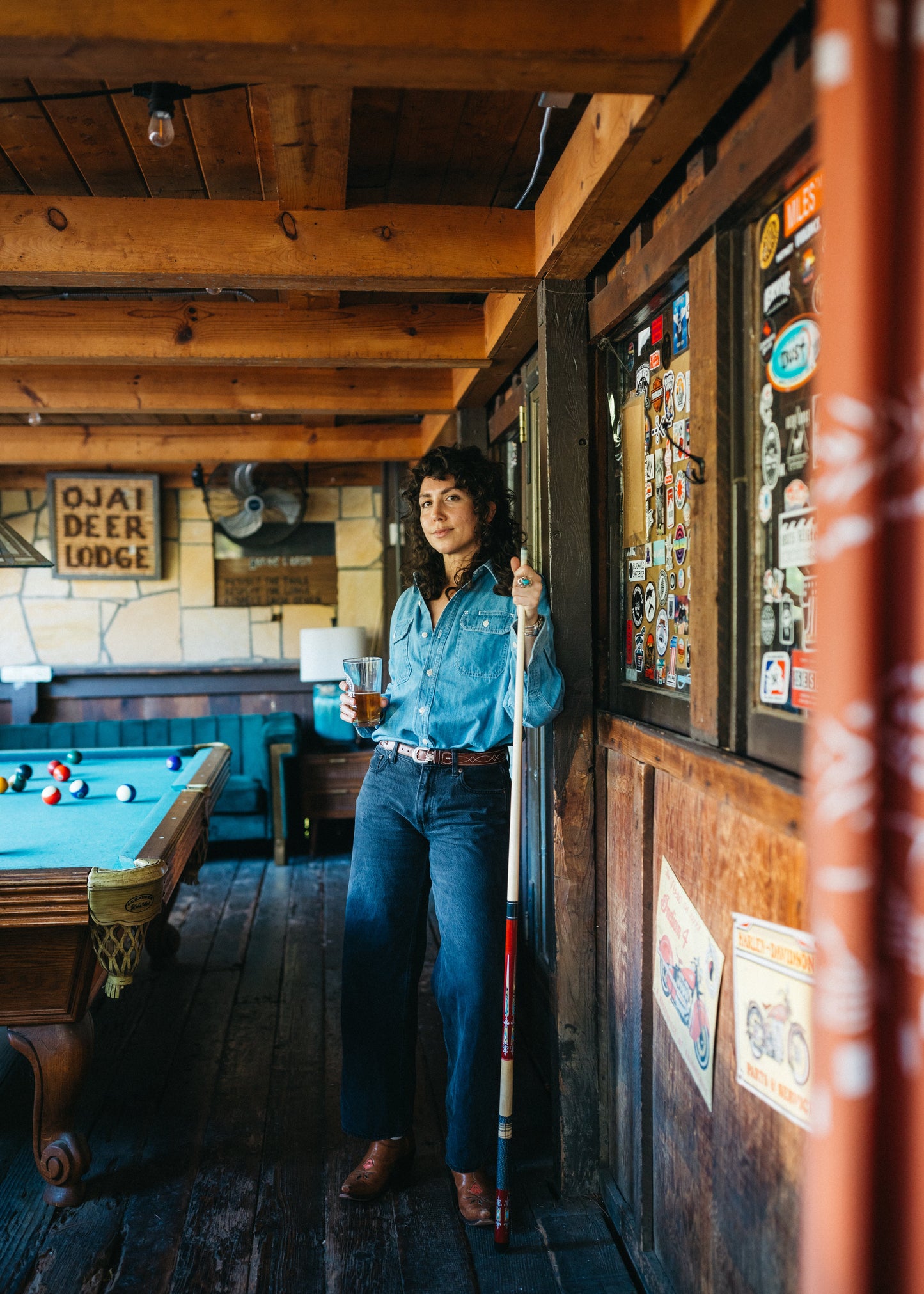Women standing in a rustic lodge with a pool table and wooden walls wearing Lone Pine Japanese light wash denim shirt