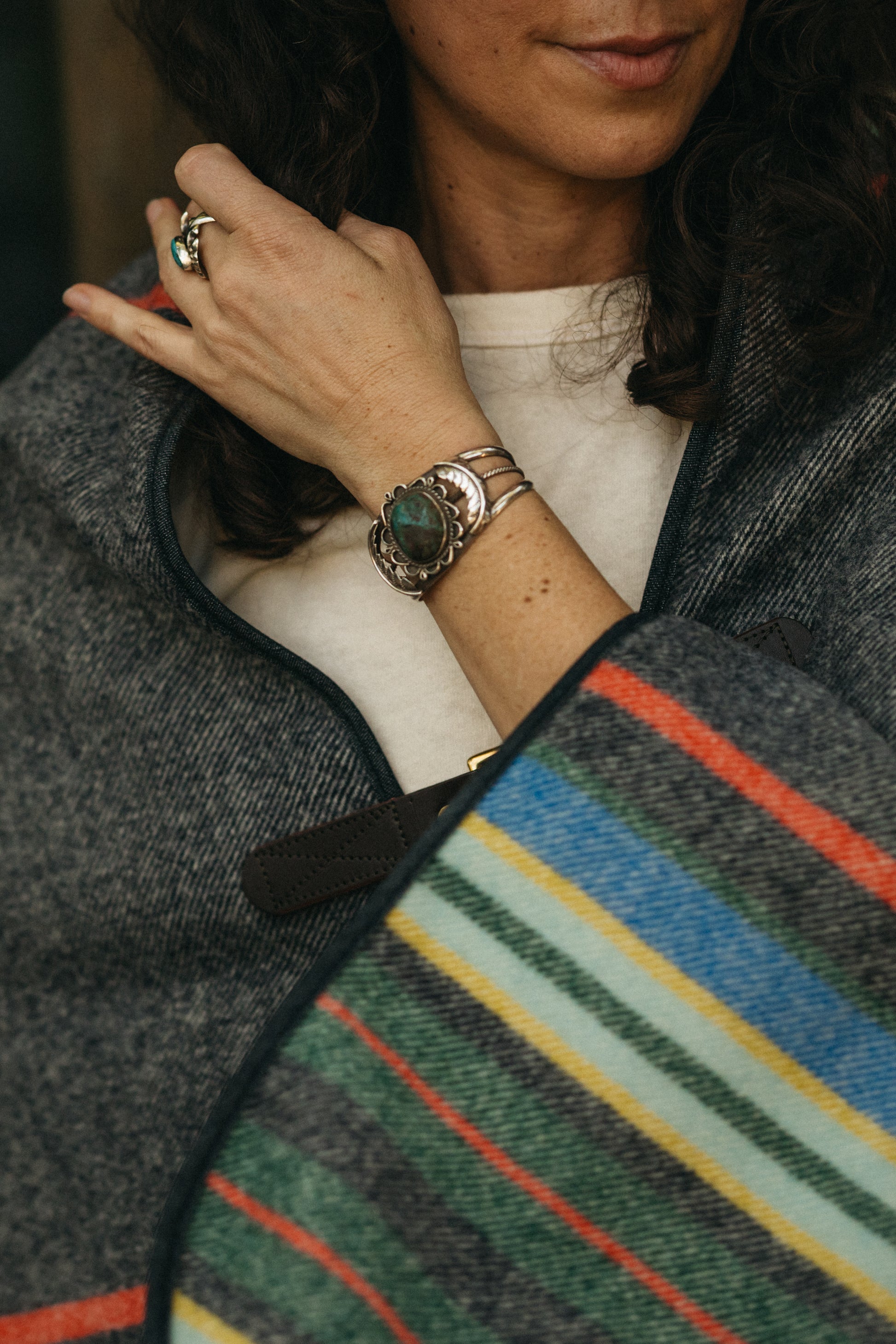 Person wearing a silver native american cuff with a colorful striped wool poncho in the foreground