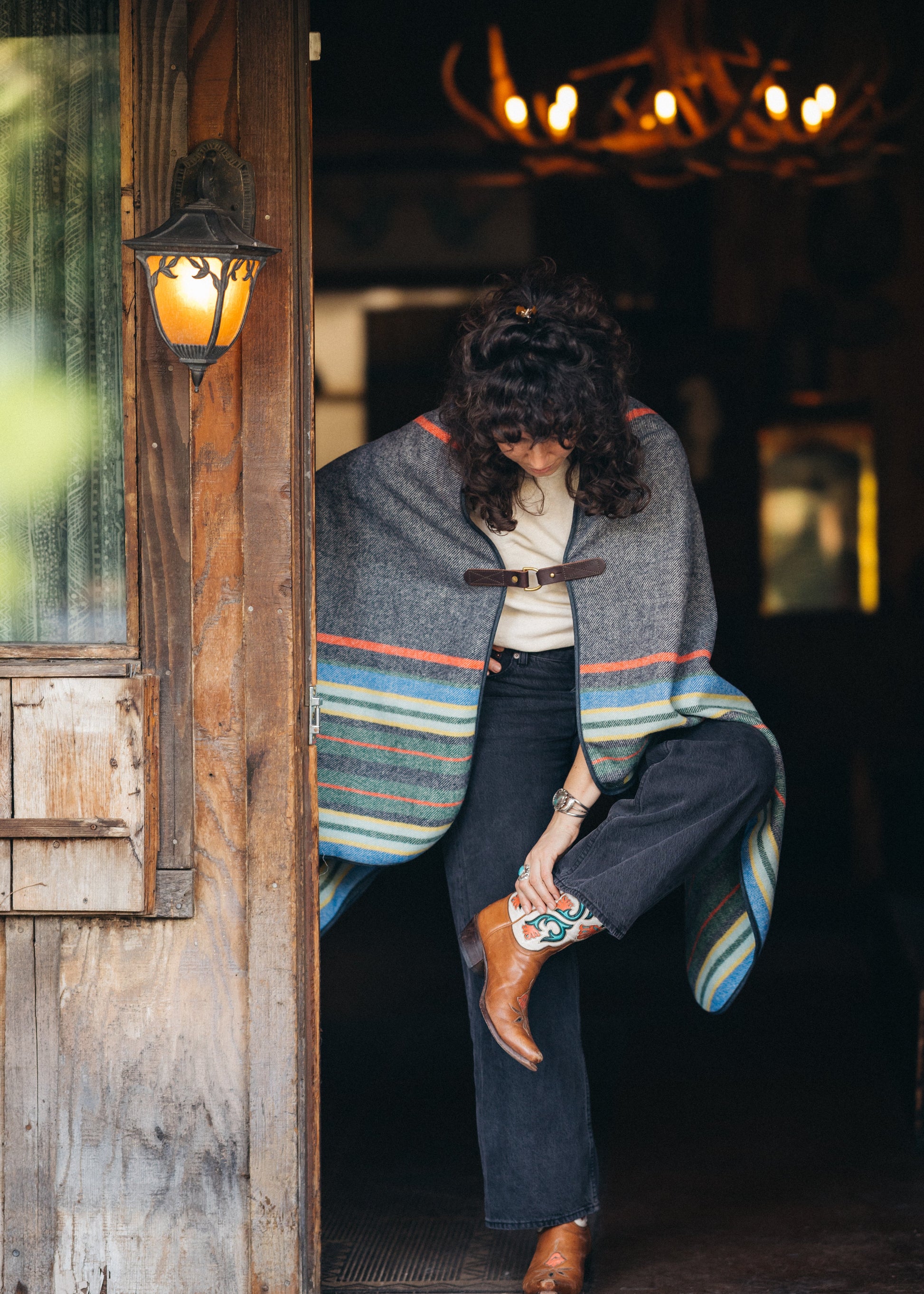 Person wearing a colorful poncho in front of a rustic wooden building.