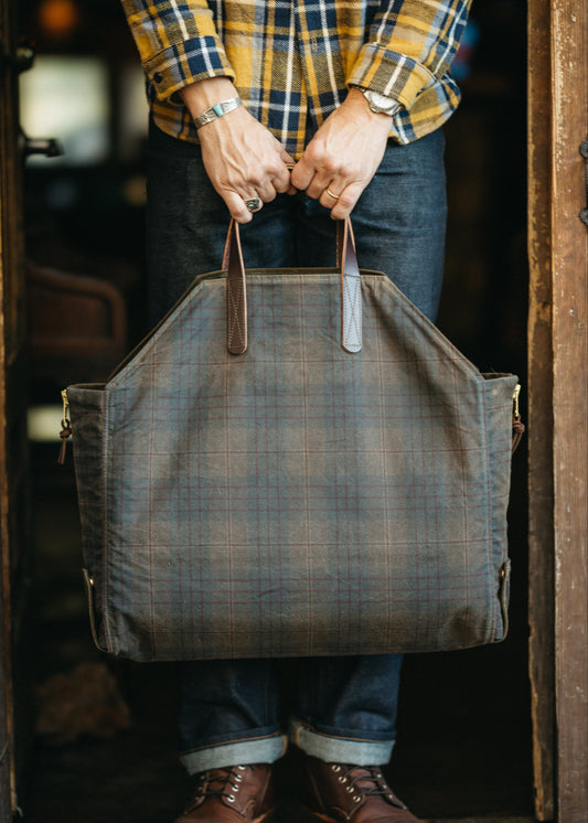 Person holding a large plaid waxed canvas convertible tote in a doorway