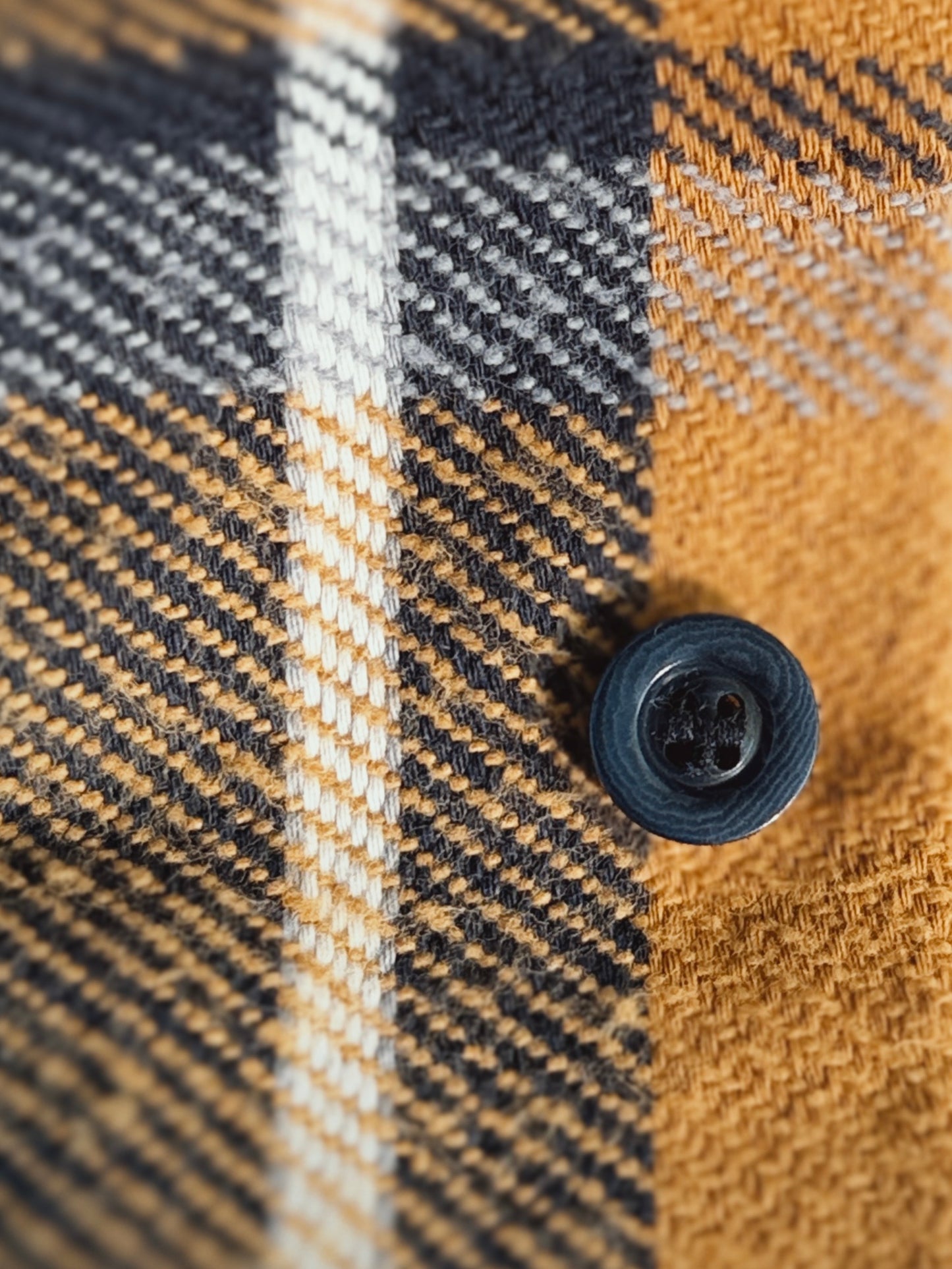Close-up of a plaid fabric with a custom dyed corozo button. Yellow, blue, grey, and white.